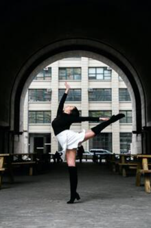 Picture of young woman in heels in a ballet pose, outside under an arch in NYC